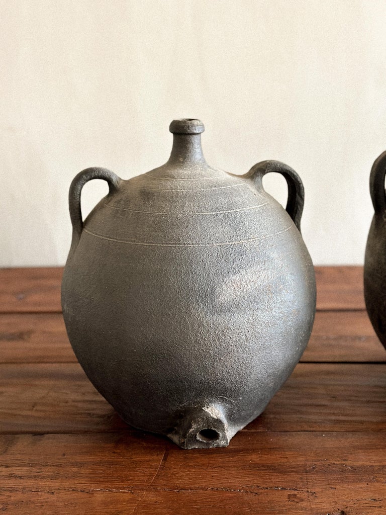 Two rustic clay vessels with darkened finish and organic form